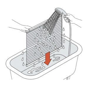 Plissee Reinigung 1.3 Eine schematische Strichzeichnung zeigt, wie ein Plissee in einer Badewanne gereinigt wird. Eine Person hält das auseinandergezogene Plissee senkrecht über die Wanne, während eine zweite Hand es mit einem Duschkopf gründlich abspült. Ein großer roter Pfeil zeigt nach unten in die Badewanne, um das Ablaufen des Wassers zu verdeutlichen.